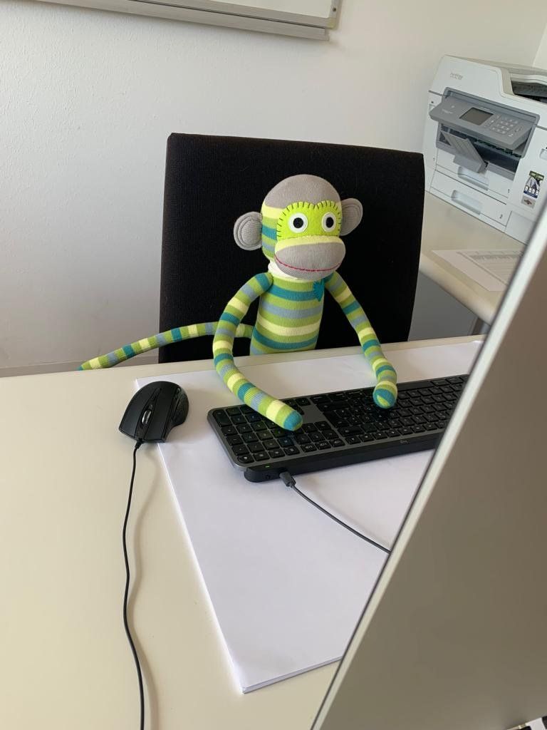 Ein ausgestopfter Affe sitzt neben einer Tastatur und einer Maus auf einem Schreibtisch.