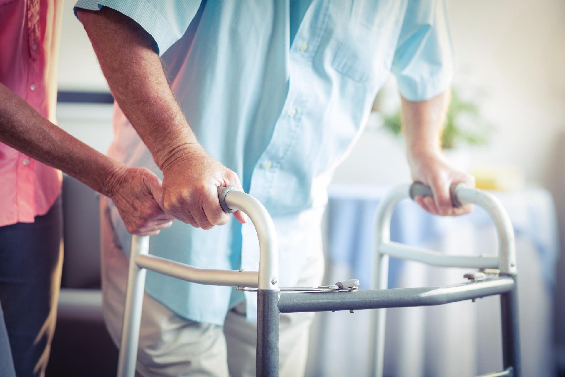Eine Frau hilft einem älteren Mann, einen Rollator zu benutzen.