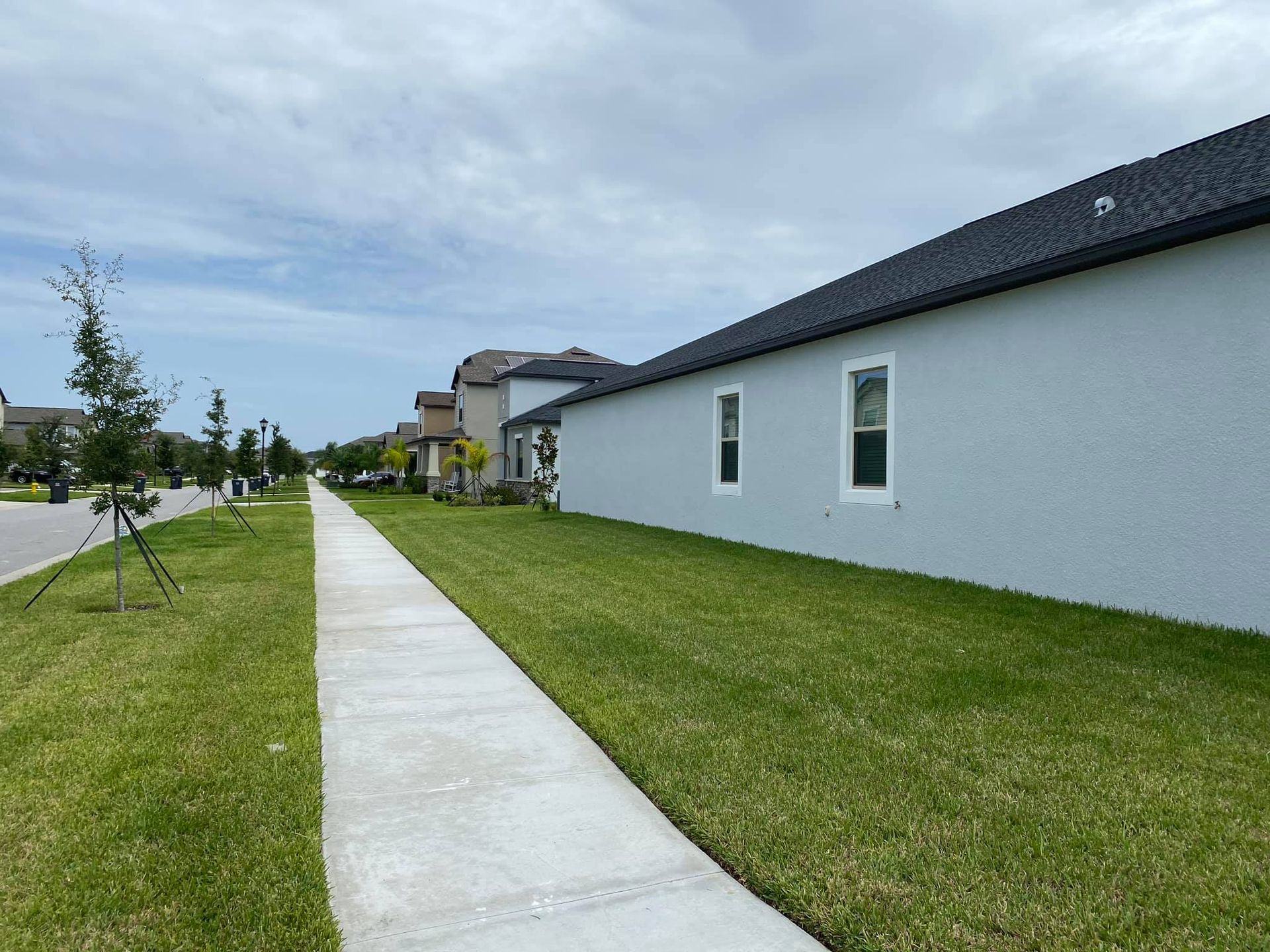 Suburban sidewalk beside green lawns and gray houses under a cloudy sky