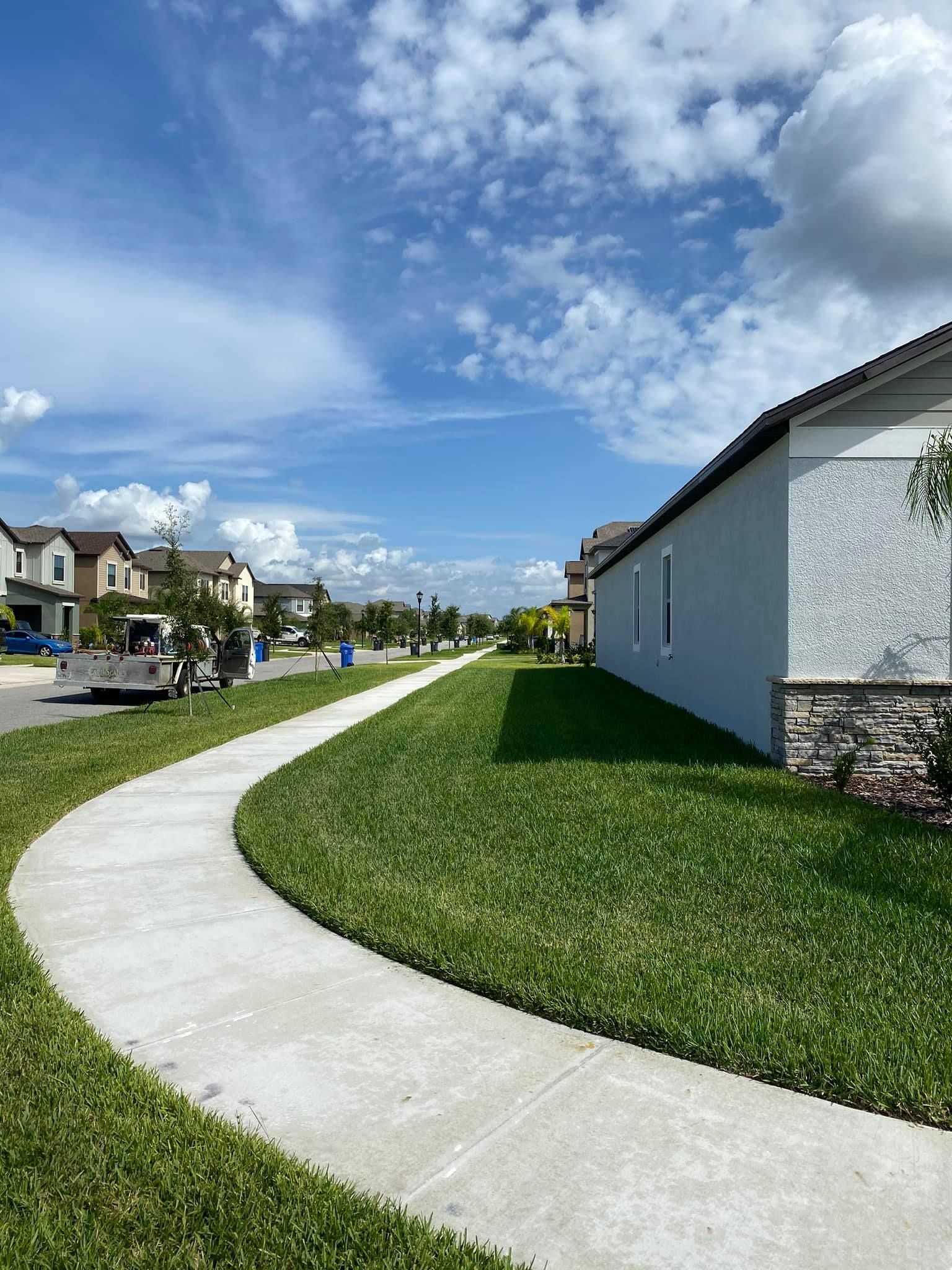 Curved sidewalk beside houses under a blue sky with scattered clouds