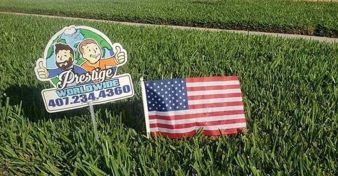 Small lawn sign and American flag standing in green grass field.