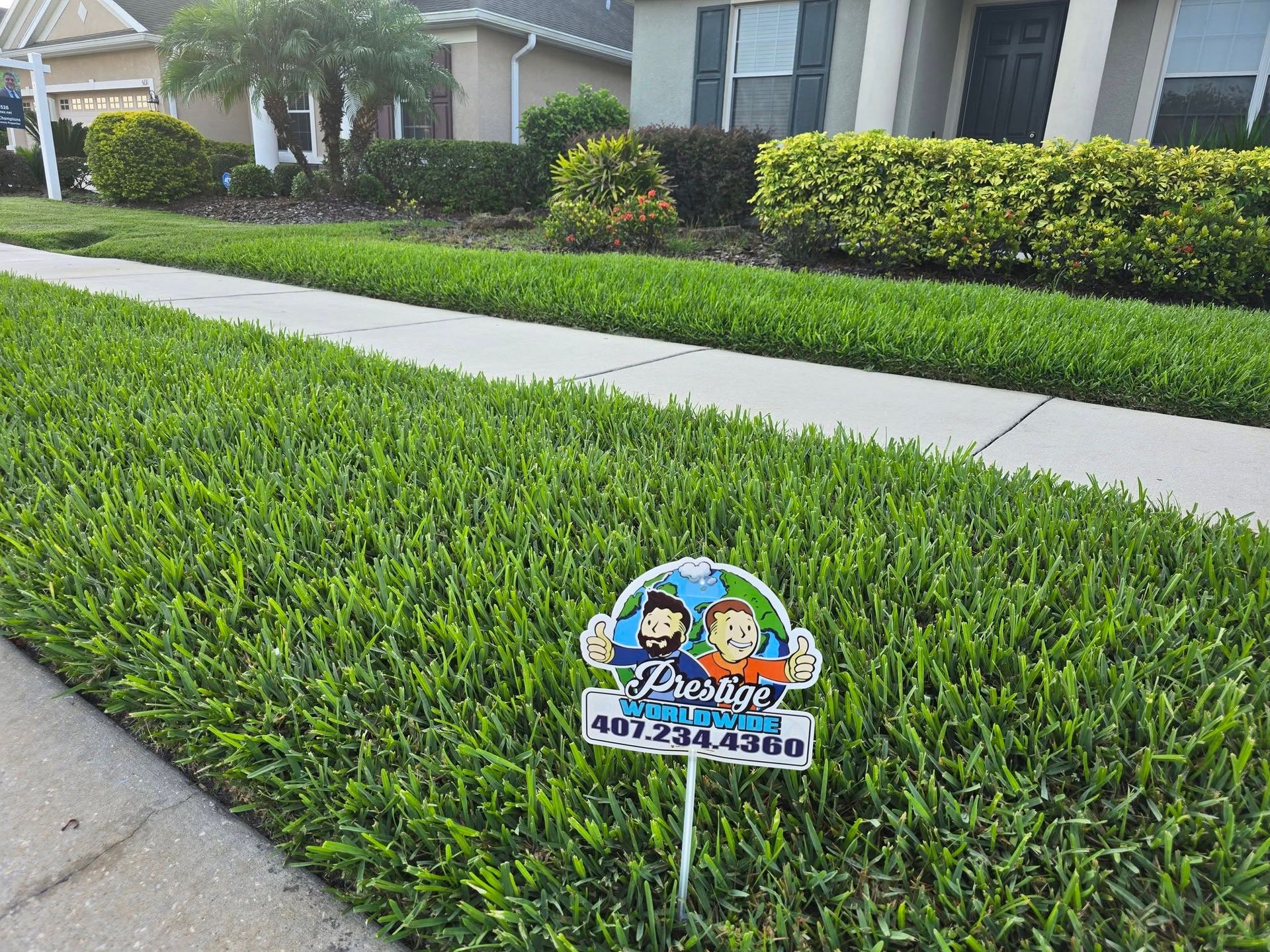 Lawn sign in a neatly trimmed front yard beside a sidewalk and suburban house.
