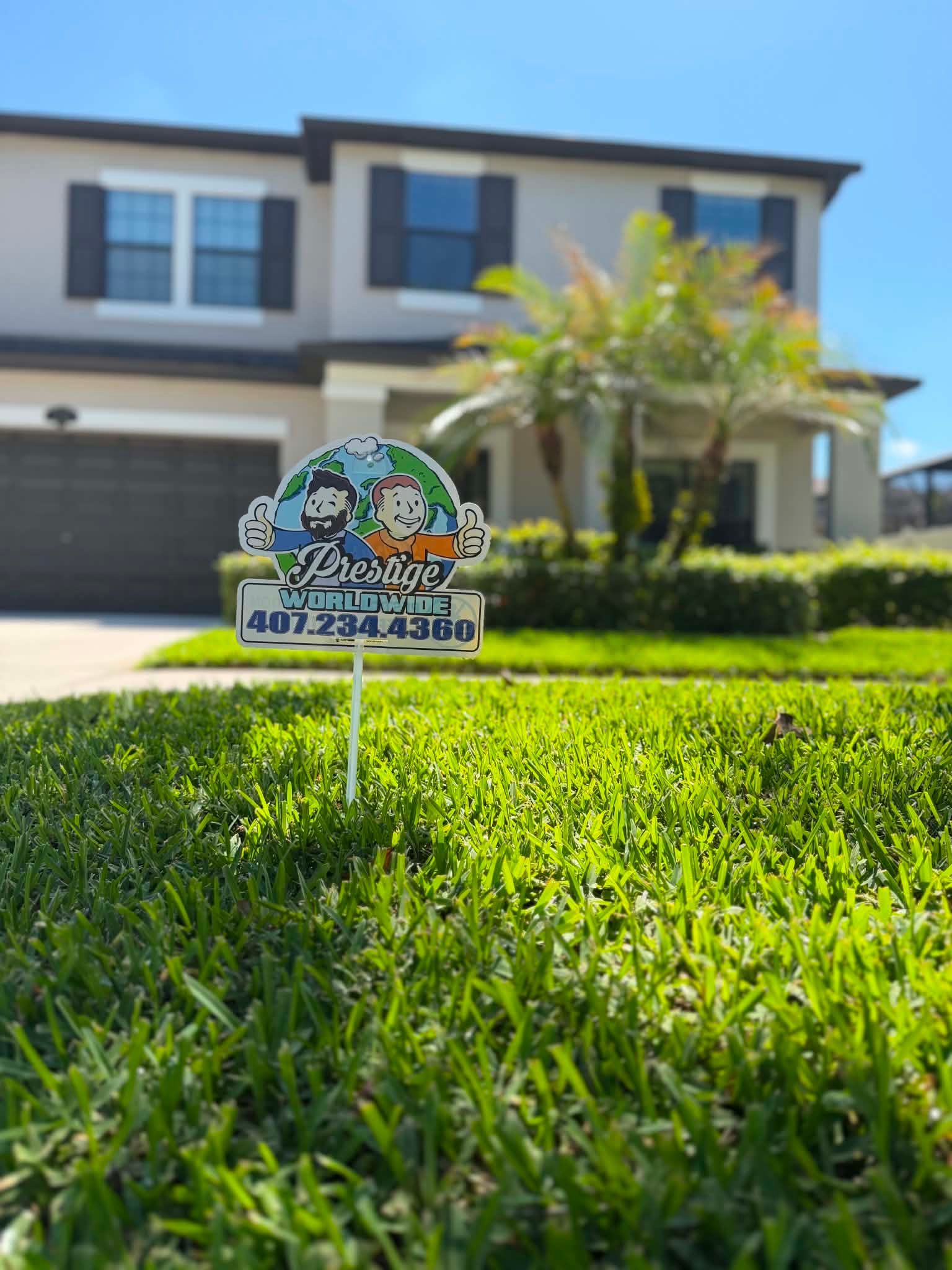 Small garden sign in bright green grass in front of a two-story house with palm trees.