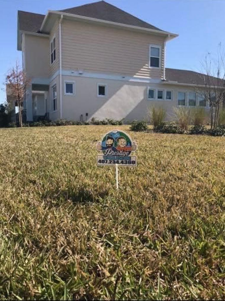 Two-story beige house with a small yard sign in the grass on a sunny day.