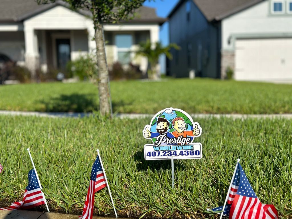 Yard sign with a cartoon logo among three small American flags in front of a suburban house.