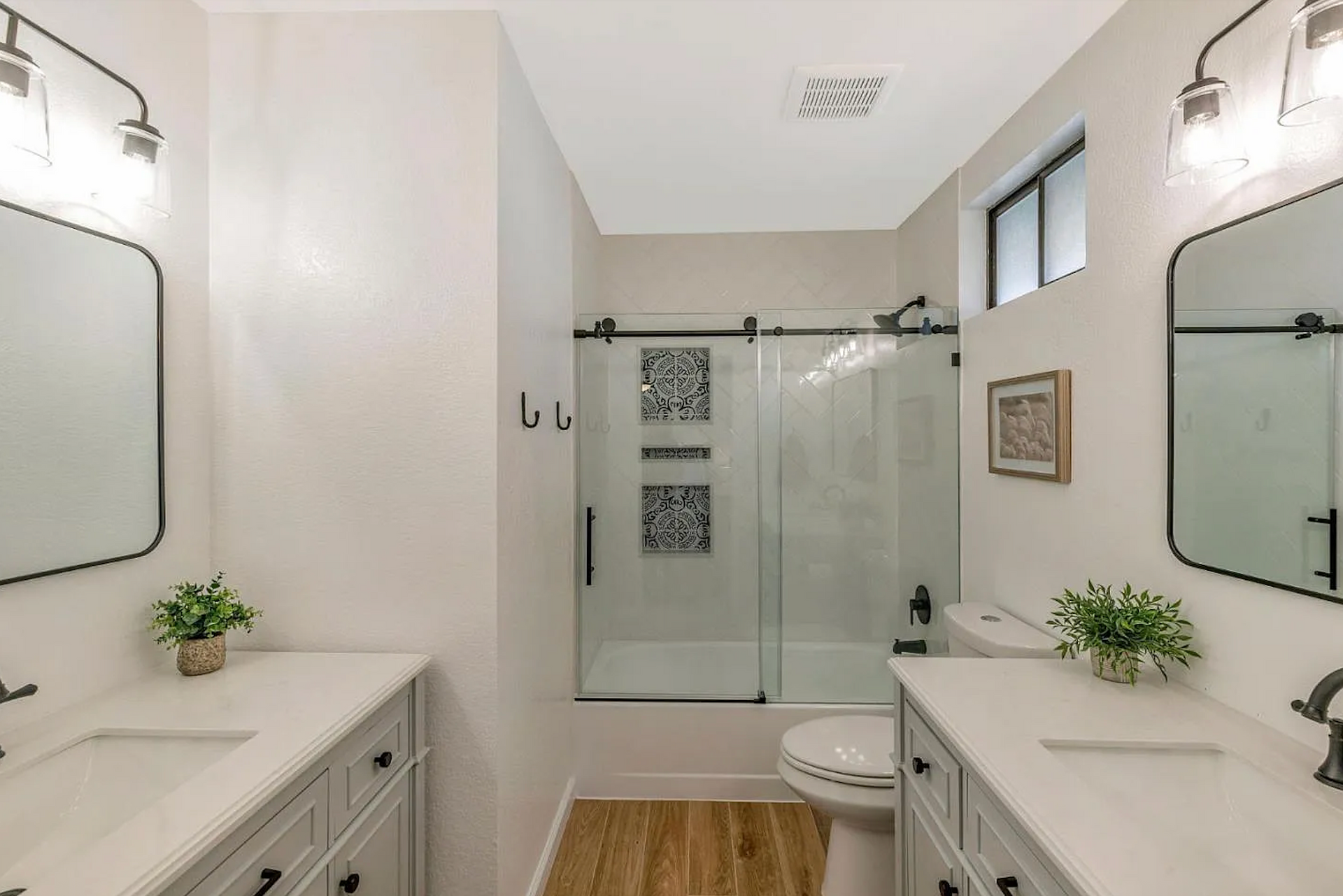 Bathroom with dual sinks, shower, and toilet; white walls, gray cabinets, black fixtures.