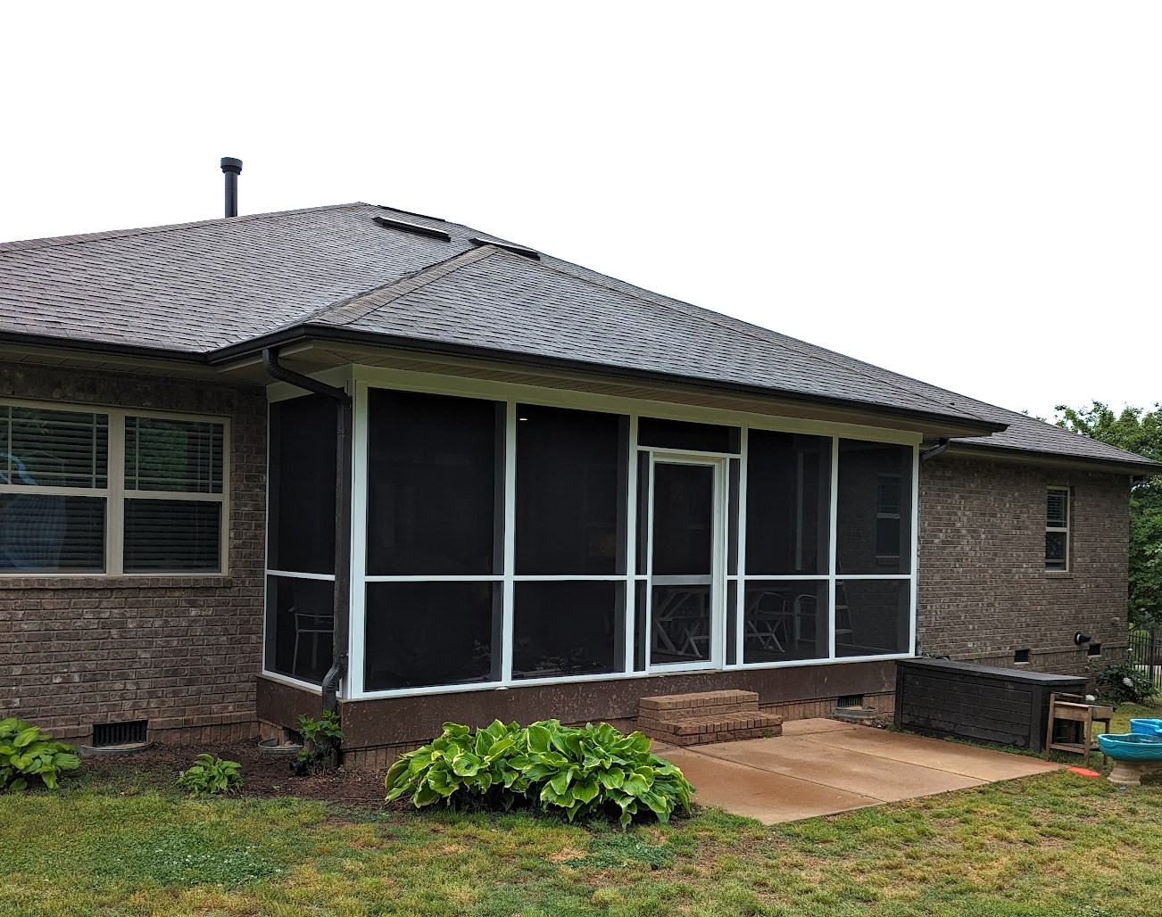 Screened-in porch on a brick house. Black screens, white trim, and a concrete patio with green foliage.