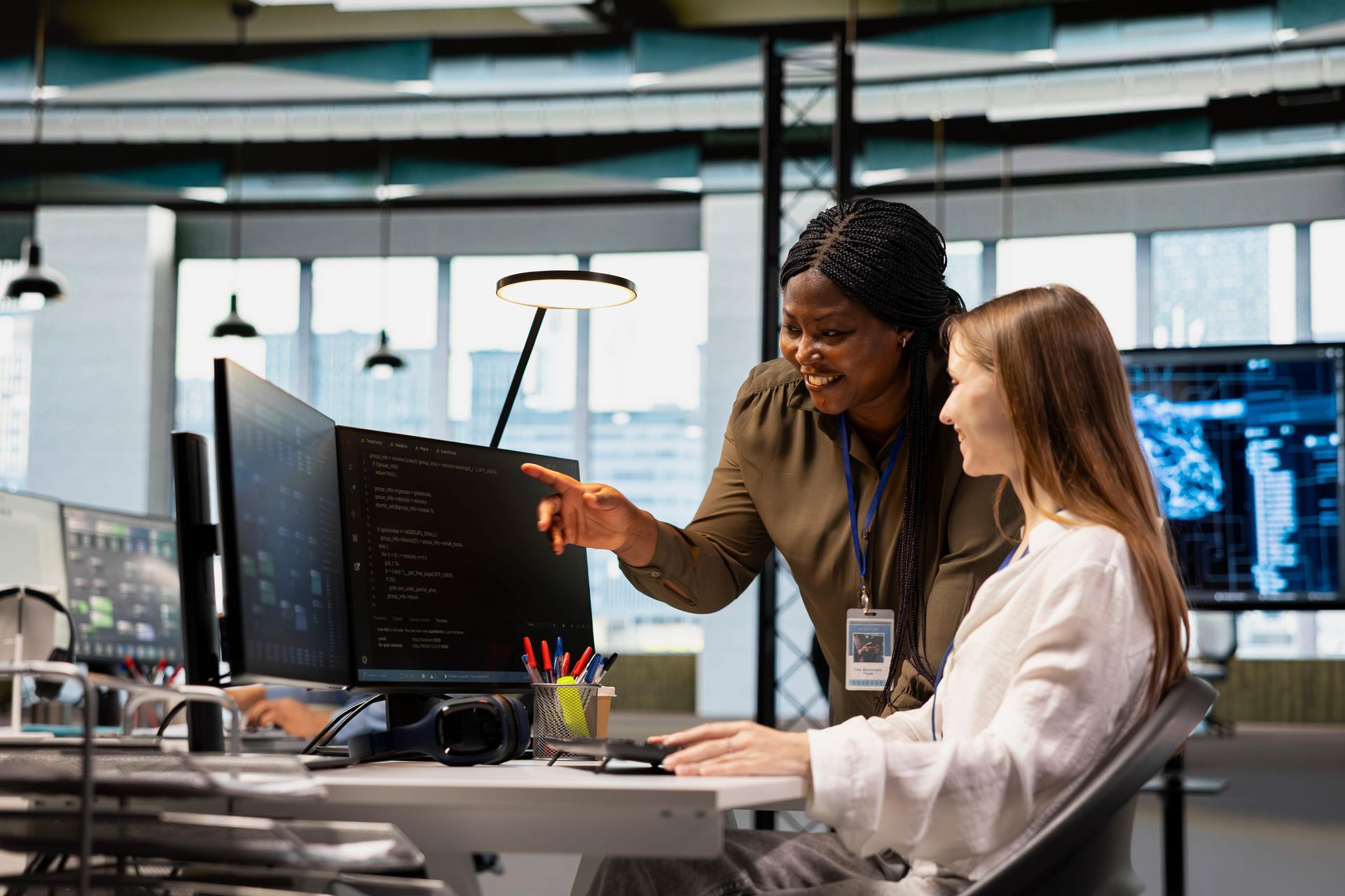 Two coworkers reviewing code on desktop monitors in a modern office