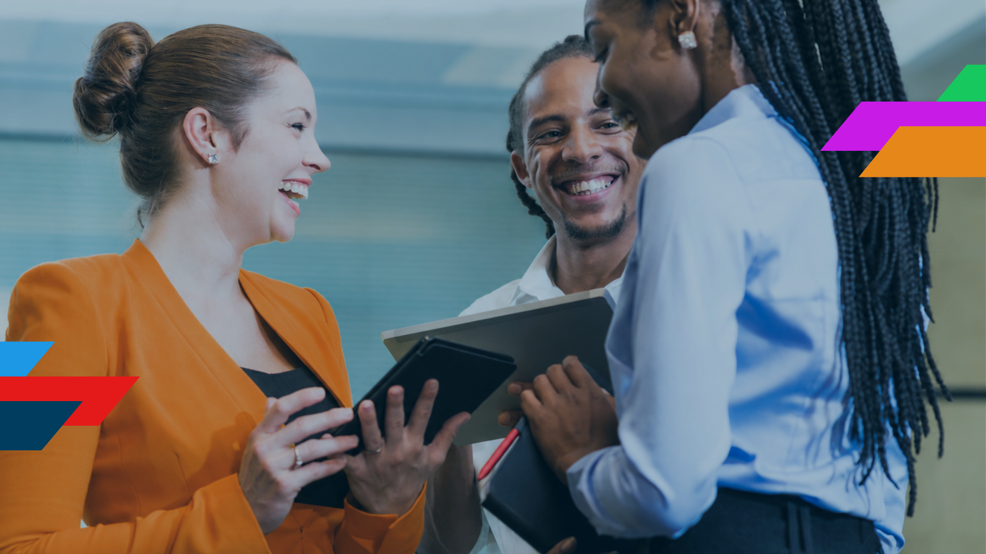 Three coworkers smiling and discussing a tablet in an office meeting