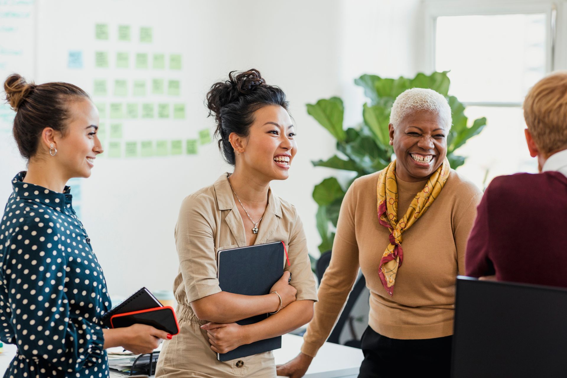 Four coworkers smiling and chatting in a bright office meeting space