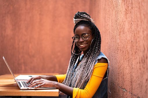 Person smiling and typing on a laptop at a wooden table against a warm orange wall