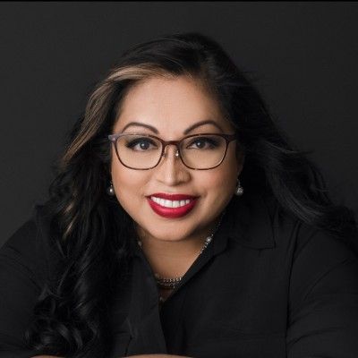 Portrait of a smiling woman with black hair and glasses, wearing black against a dark background
