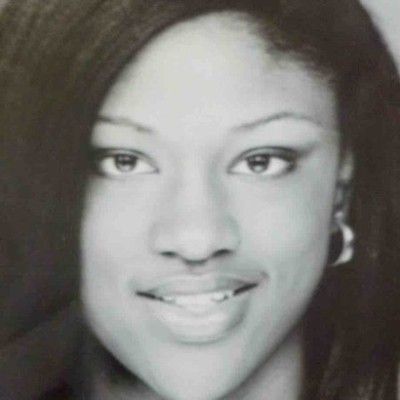 Black-and-white close-up portrait of a person smiling softly, with long hair and hoop earrings