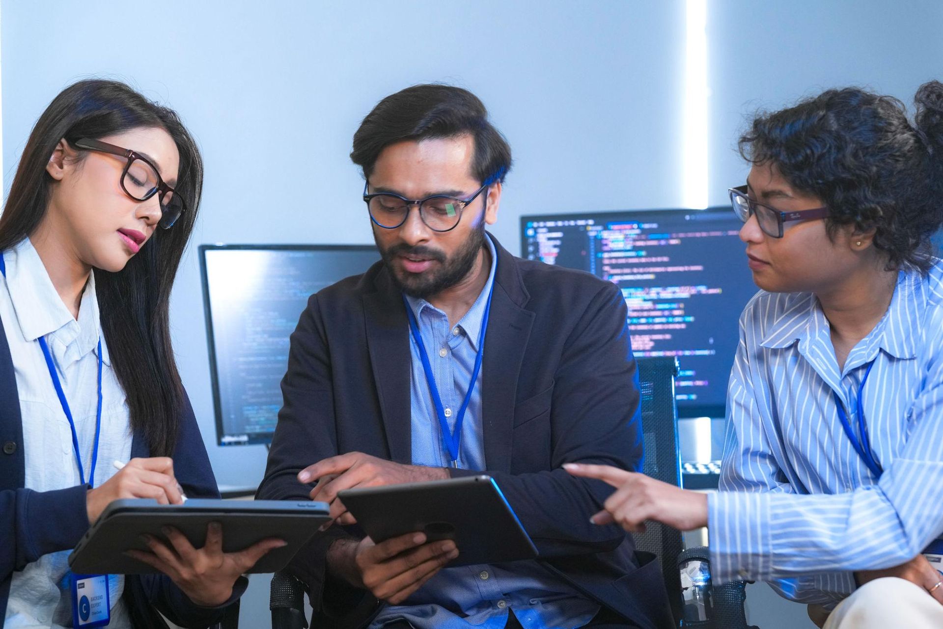 Three coworkers reviewing a tablet and laptop in front of computer monitors in an office