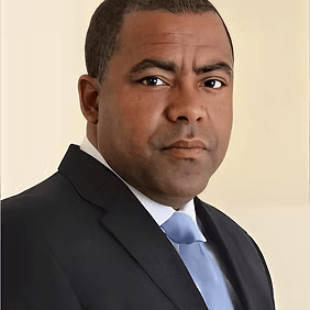 Formal portrait of a man in a dark suit and light blue tie against a neutral background