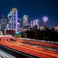 Night city skyline with lit skyscrapers and a glowing ferris wheel above light trails on a highway