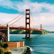 Golden Gate Bridge spanning blue water under a clear sky, viewed from the shore with a cliffside in foreground