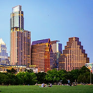 City skyline with tall modern buildings and a grassy park under a clear blue sky