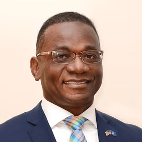 Smiling man in a navy suit, white shirt, patterned tie, and glasses against a light background
