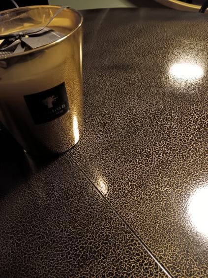 Una tazza di caffè su un tavolo lucido e maculato, sotto una calda luce artificiale.