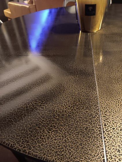 Primo piano di un tavolo decorato con l'ombra sfocata di una mano e una tazza dorata sullo sfondo.