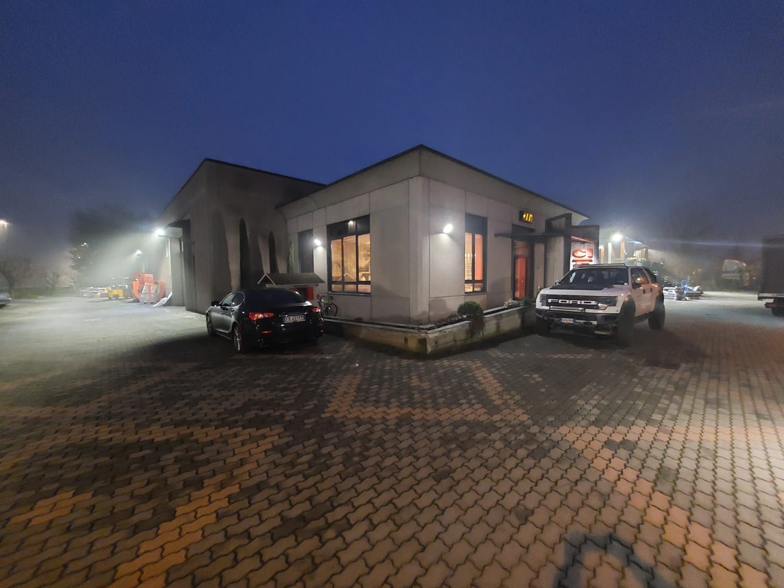 Parcheggio nebbioso fuori da un edificio illuminato con due auto parcheggiate al crepuscolo