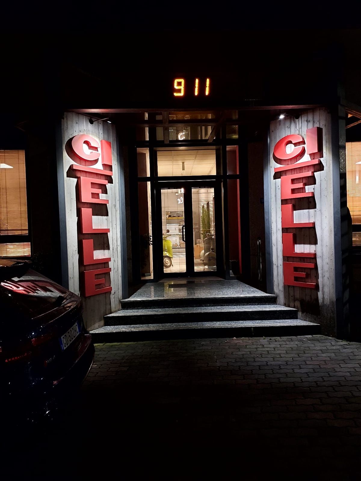 Ingresso notturno di un edificio con insegne verticali rosse e la scritta luminosa