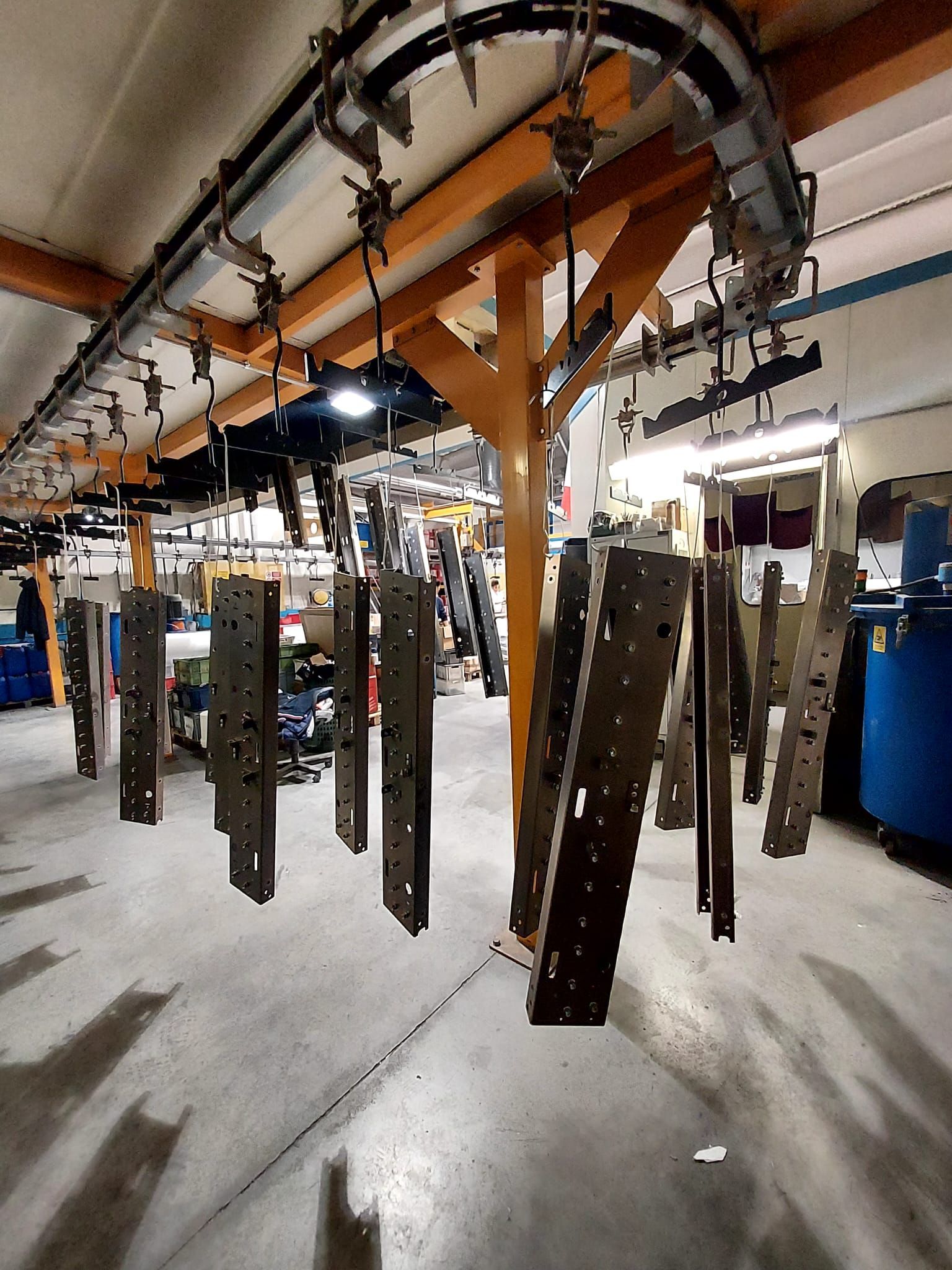 Linea di produzione industriale con pezzi metallici sospesi che si muovono su binari di trasporto aerei.