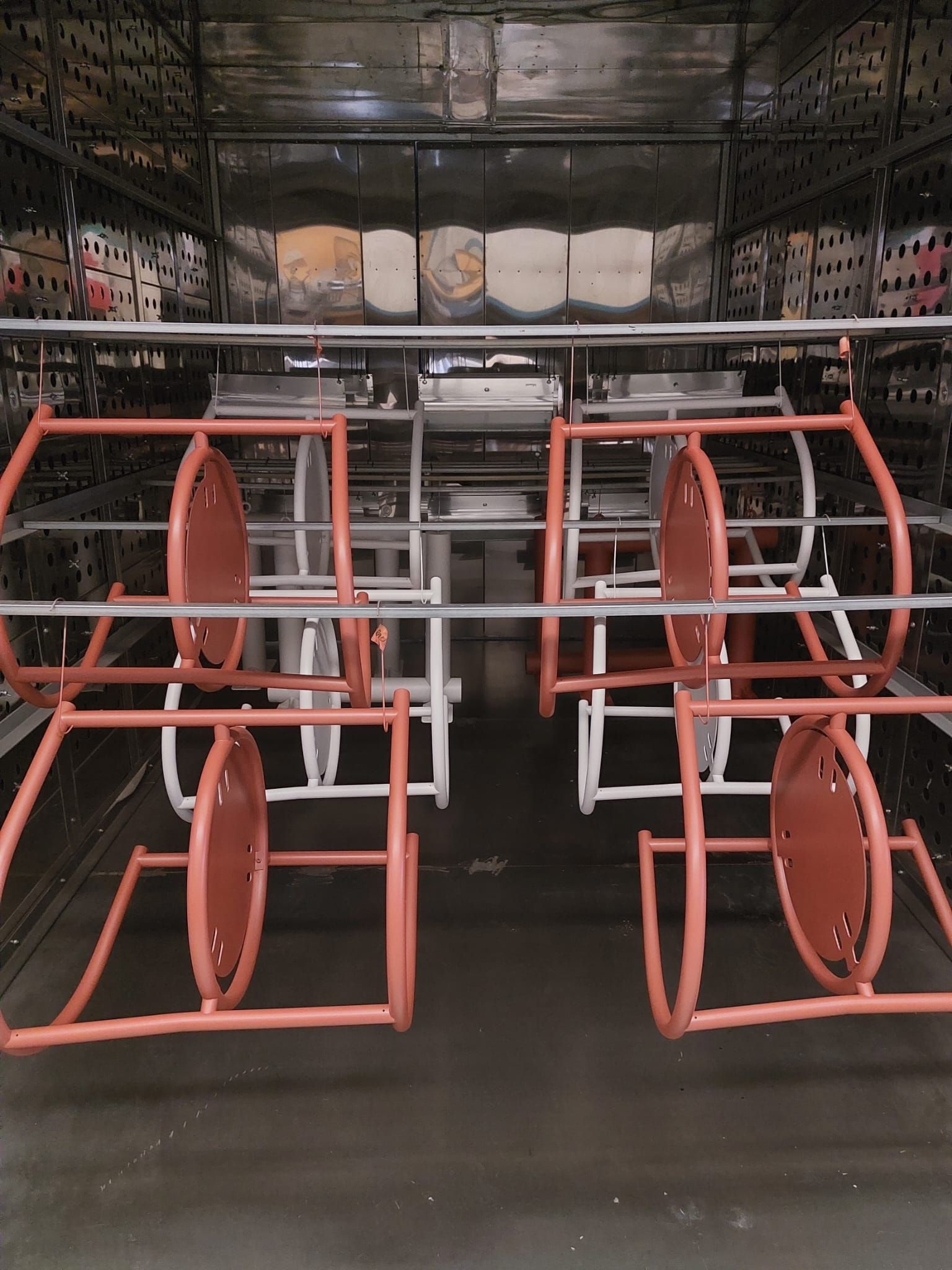 In un corridoio di un magazzino, rastrelliere metalliche rosse per bobine di cavi, con grandi bobine nere alle loro spalle.