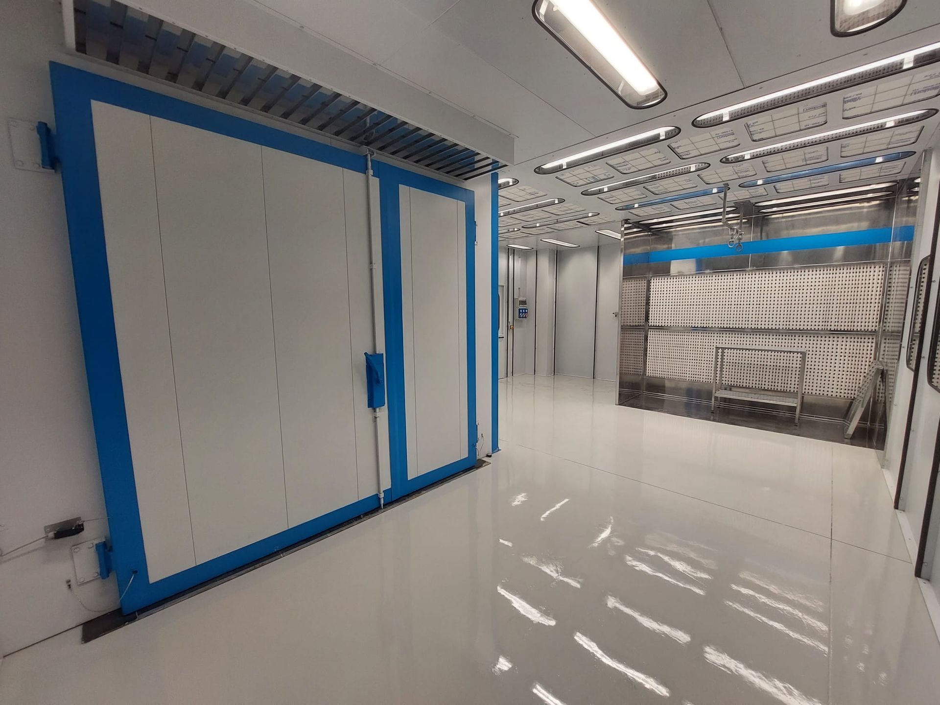 Corridoio industriale bianco e luminoso con ante degli armadi e luci a soffitto con profili blu.