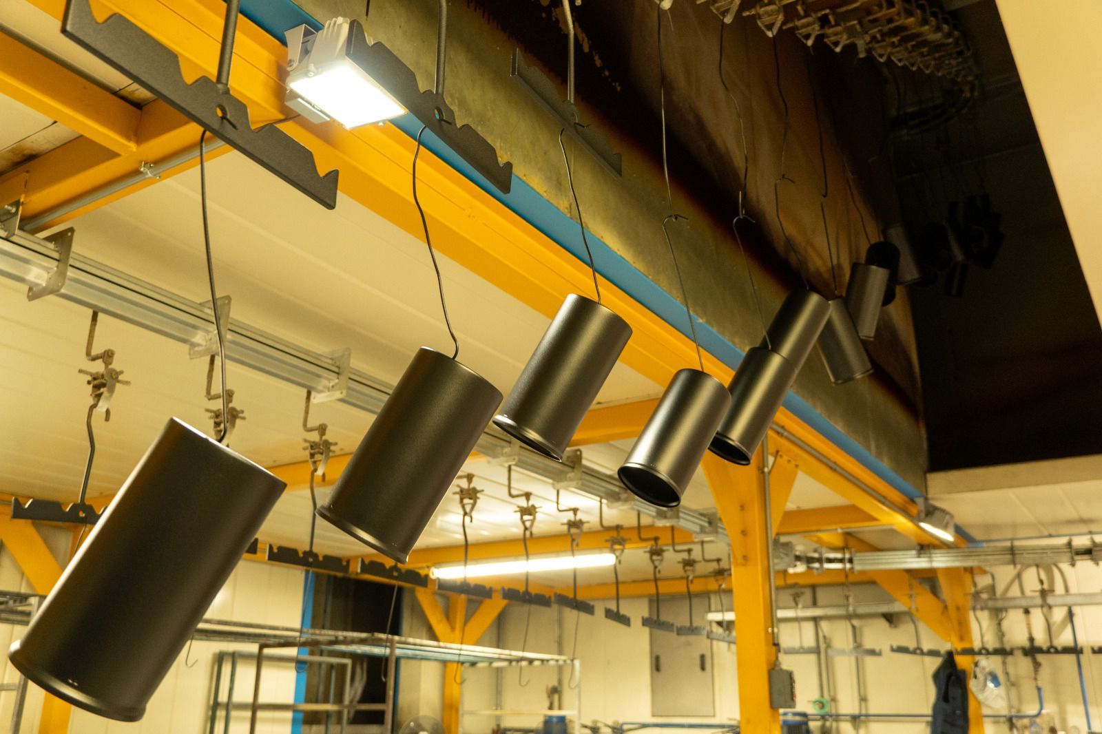 Lampade cilindriche nere sospese a travi gialle del soffitto in un interno industriale