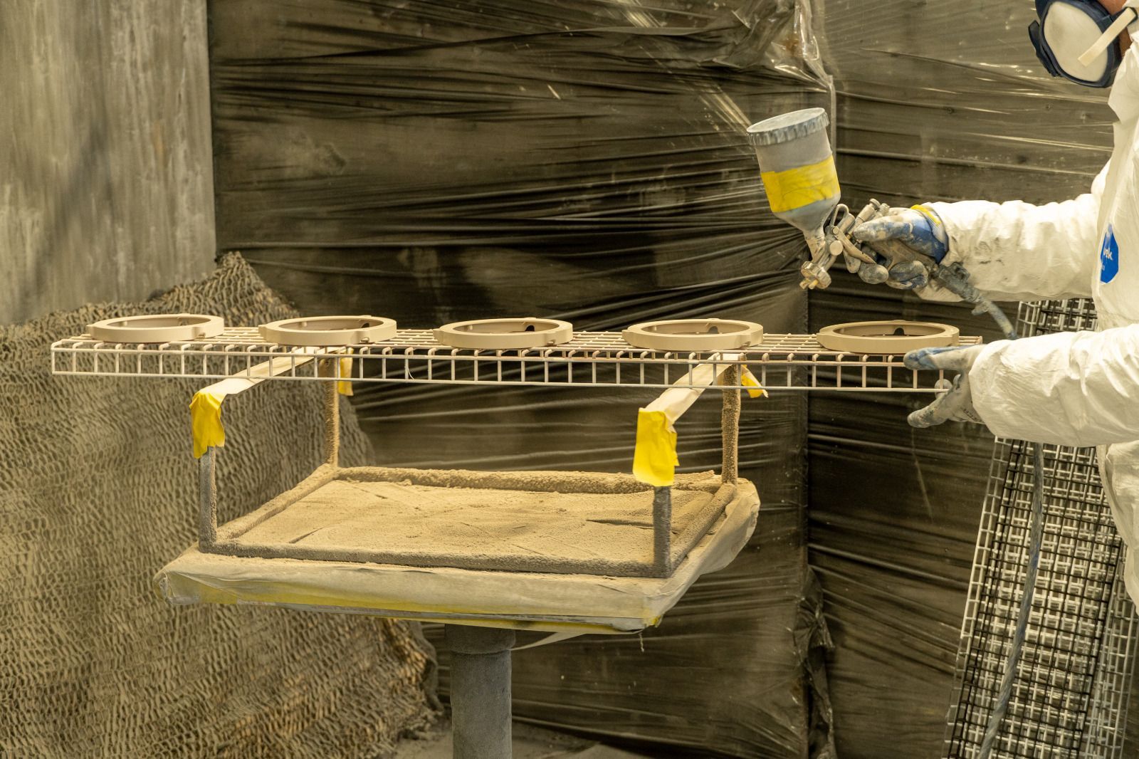 Una persona con indumenti protettivi vernicia a spruzzo uno scaffale metallico in un'officina.