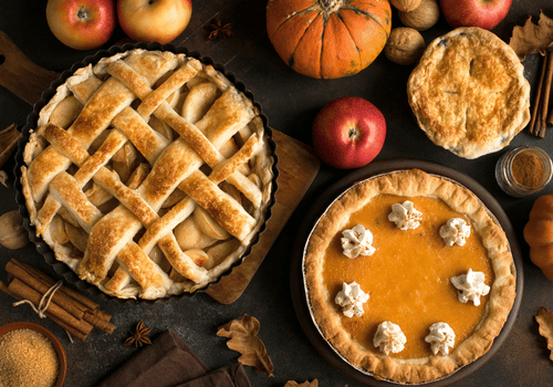 Assorted fall pies and apples on a rustic table, including lattice and pumpkin pies