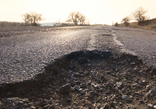 Large pothole and broken asphalt on a rural road at sunset