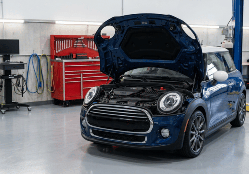 Blue MINI Cooper with the hood open inside a clean, modern auto repair shop