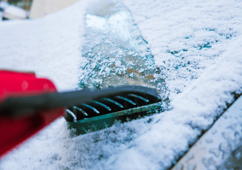 Car scraper clearing ice from a car windshield in snow