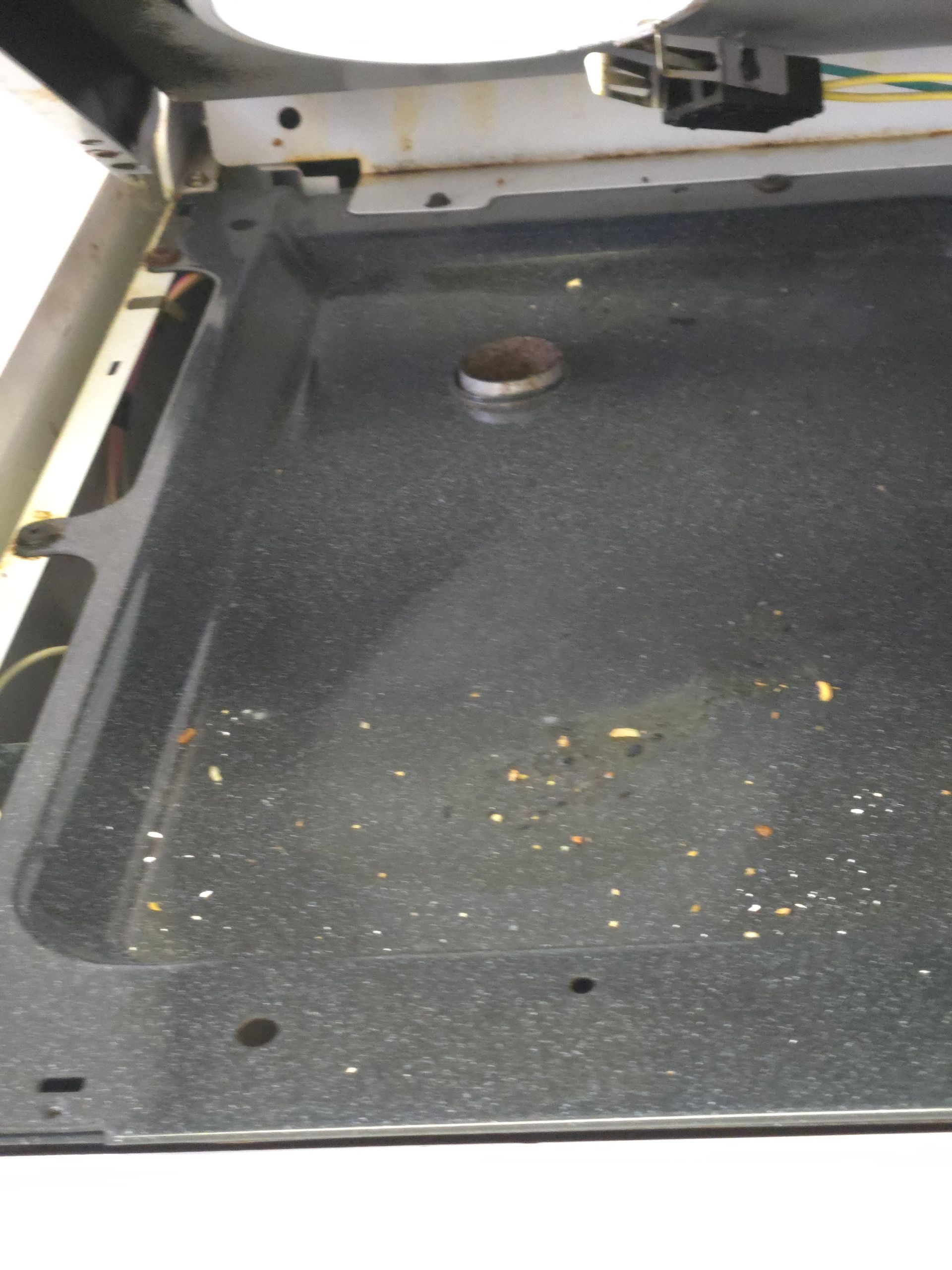 The inside of a dirty oven with food crumbs. The black oven floor has a circular metal piece and a few small holes.