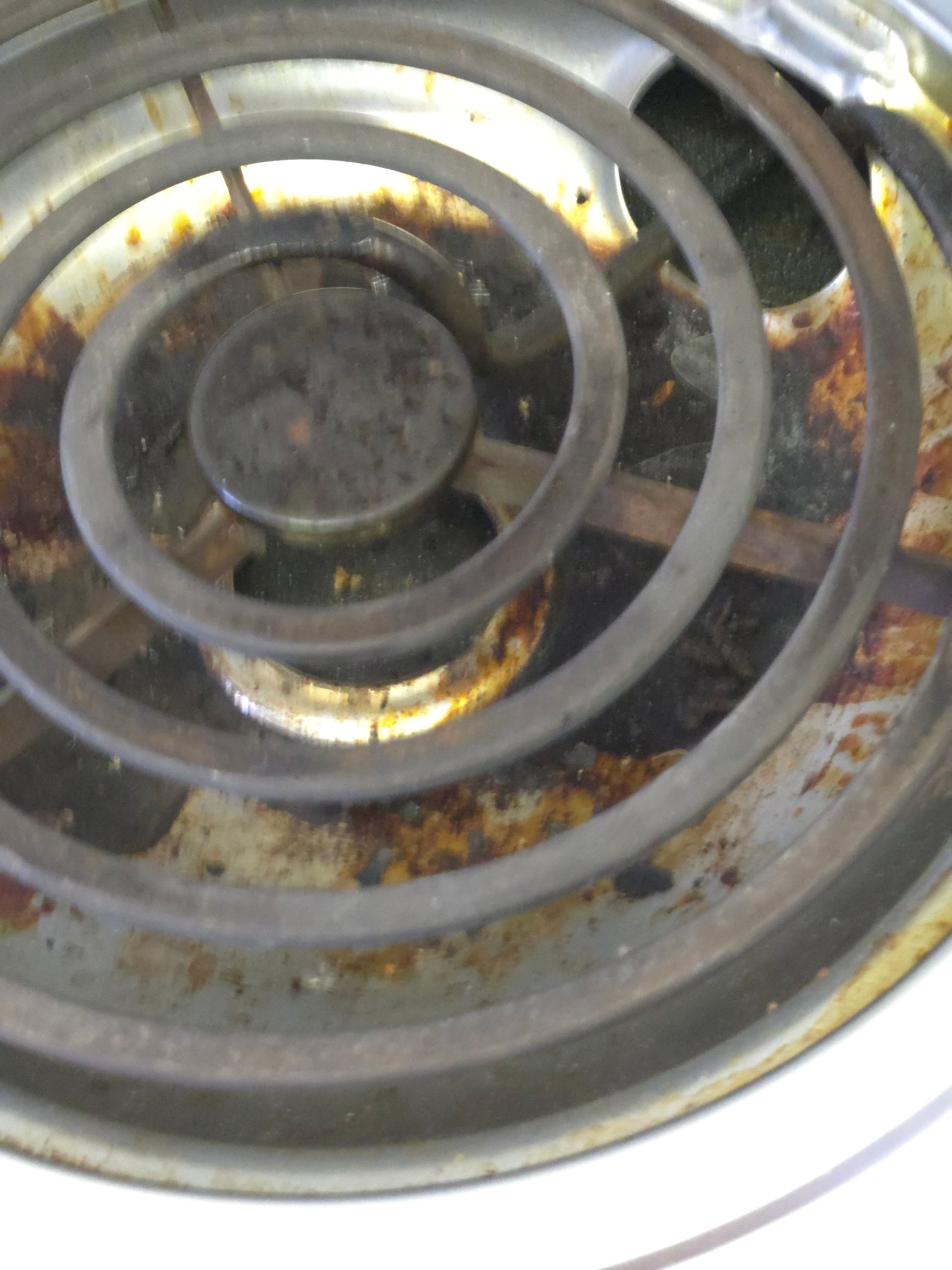 Close-up of a dirty electric stove coil with brown and black stains.