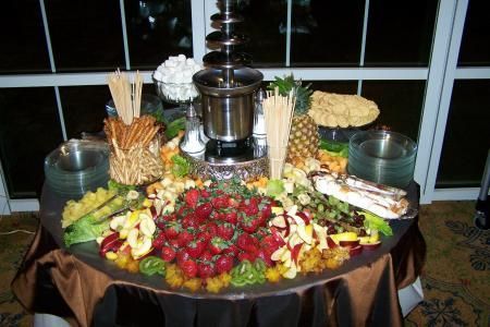 Fruit and bread buffet table with a chocolate fountain centerpiece and flowers