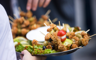 Plates of skewered appetizers with lettuce and tomato on a table, with hands serving food in the background