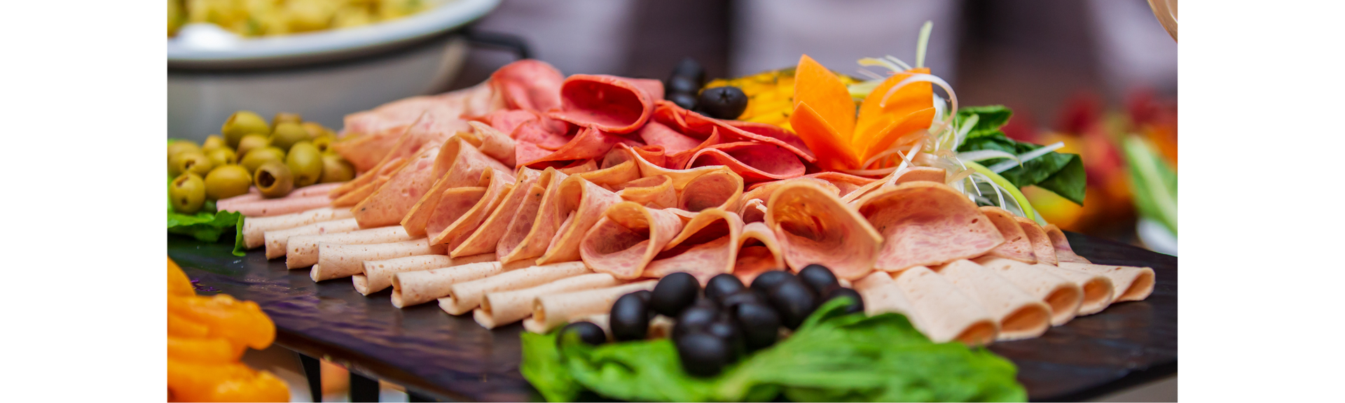 Assorted sliced deli meats and olives arranged on a wooden board with garnishes