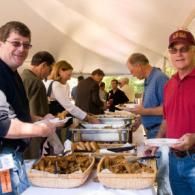 People serving food at a buffet table under a white canopy