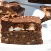 Close-up of a chocolate brownie topped with frosting and marshmallow pieces on a white plate