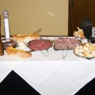 Buffet table with assorted meats, bread, and cheese on white tablecloth