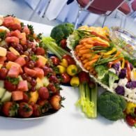Assorted fresh fruits and vegetables arranged on platters at a buffet table.