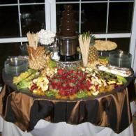 Dessert buffet table with chocolate fountain, fruit, and pastries on a black-and-brown draped table