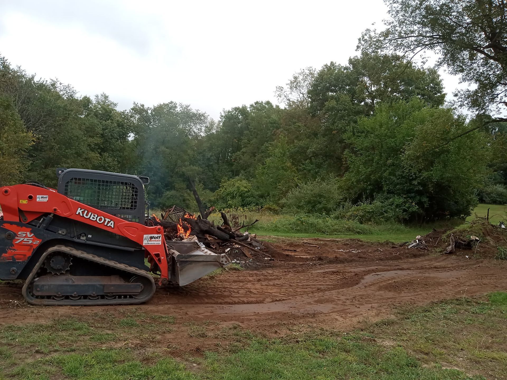 A bulldozer is moving dirt in a field with trees in the background.
