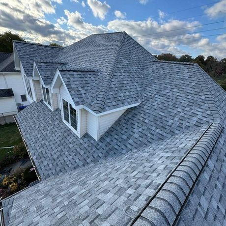 Gray shingle roof on a house with white dormers under a cloudy sky.