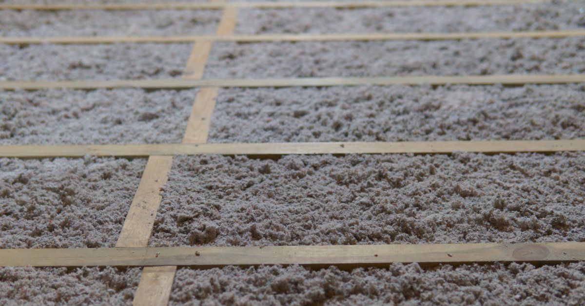 A close-up of gray, loose-fill, cellulose insulation in between thin wood strips that run horizontal