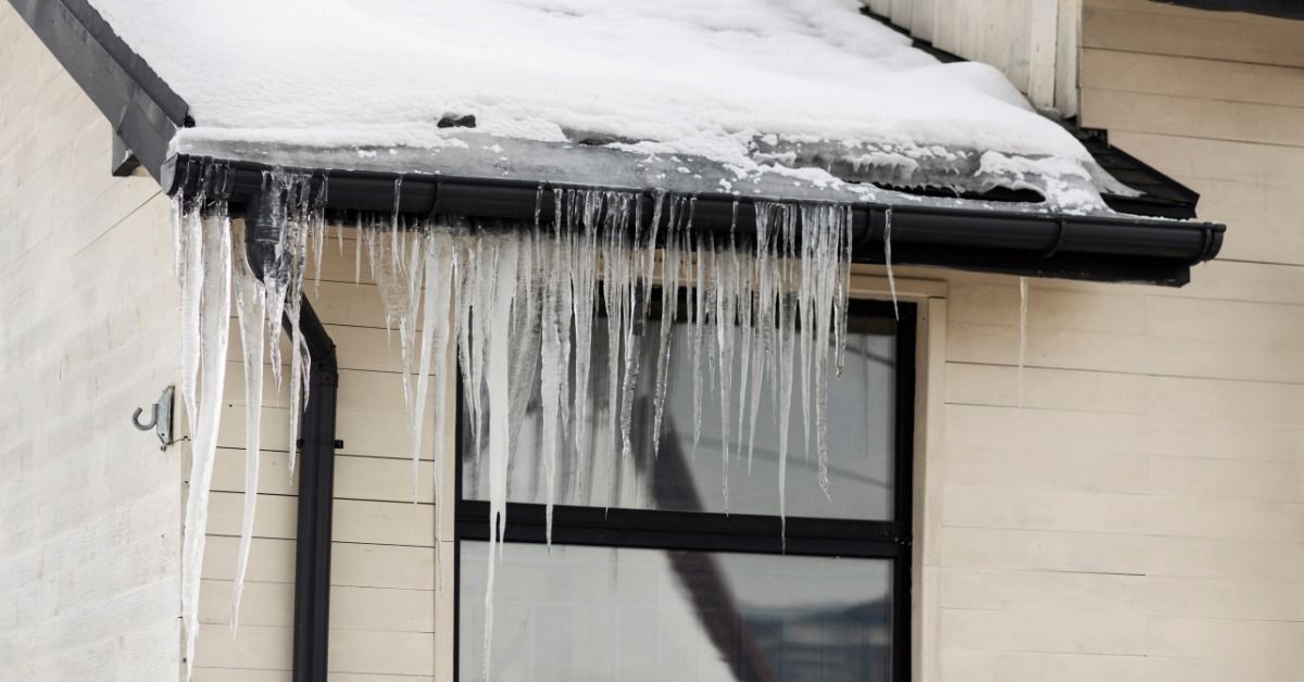 Close-up of a roofline and a window just beneath it. Snow is on the roof, and icicles hang from the gutter.